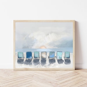 May include: A framed art print depicts a beach scene with seven blue beach chairs in a row on the sand, facing the ocean. The sky is a mix of light blue and white, with a hint of the sun setting on the horizon. The artwork is in a wooden frame.