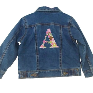 May include: A blue denim jacket with a floral letter A embroidered on the back.