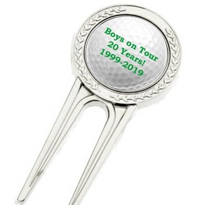 May include: Silver golf ball retriever with a white golf ball design. The golf ball has the text "Boys on Tour 20 Years! 1999-2019" in green.