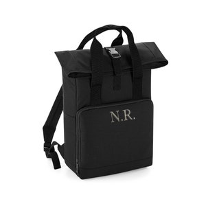 May include: Black roll top backpack with a zipped front pocket and adjustable straps. The backpack has a silver buckle and the initials "N.R." embroidered on the front.
