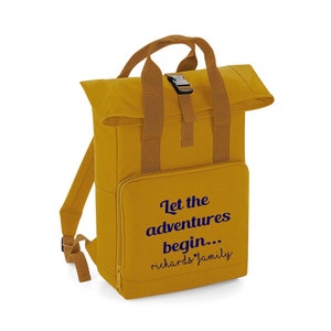 May include: A mustard yellow canvas backpack with brown straps and a buckle closure. The backpack has a flap that folds over the top and is secured with a zipper. The front of the backpack has a navy blue embroidered design that says "Let the adventures begin... Richards Family".