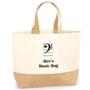 May include: A white canvas tote bag with brown jute trim. The bag has a black treble clef and the text "Alex's Music Bag" printed on it.