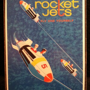 May include: A vintage poster advertising the Rocket Jets ride at Tomorrowland. The poster features a blue background with a yellow and red rocket ship flying through the air. The text on the poster reads "Rocket Jets, Fly One Yourself, Tomorrowland".