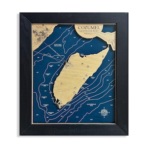 May include: Framed wooden map of Cozumel, Quintana Roo, Mexico. The map features a detailed depiction of the island with depth contours in blue against a blue background. The frame is black.