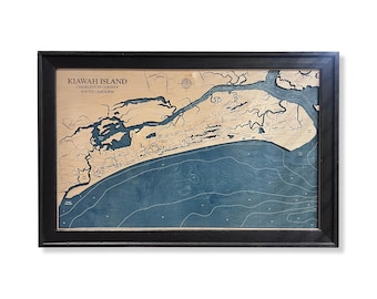 May include: A framed wooden bathymetric map of Kiawah Island, Charleston County, South Carolina. The map features a light wood landmass against a deep blue water background with engraved topographical lines and a compass rose detail.