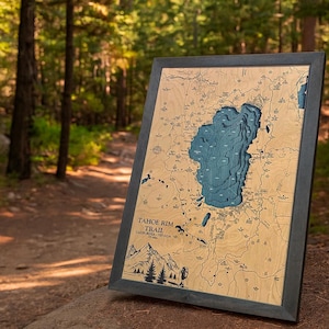 May include: A framed wooden map of Lake Tahoe, with a blue lake and surrounding terrain carved into the wood. The map is labeled "Tahoe Rim Trail" and includes a mountain graphic. The frame is dark gray.