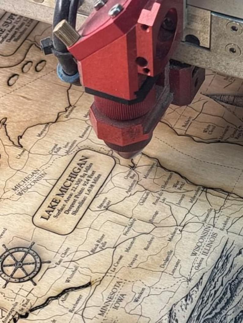 A red laser cutter is cutting a map of Michigan, with the text "LAKEMIGAN" visible on the map.