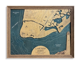 May include: A framed wooden bathymetric map of Cape May Point, New Jersey, featuring layered light wood landmasses against a deep blue water background. The map includes engraved text, geographic labels, and a lighthouse illustration.