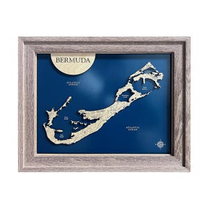 May include: Framed wooden map of Bermuda with a blue background. The map is a detailed relief carving, showing the island's shape and key locations. The frame is a light gray color, and the text "BERMUDA" is at the top.