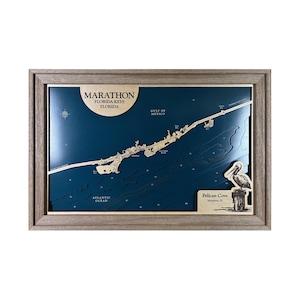 May include: A framed wooden map of Marathon, Florida Keys, with a dark blue background. The map shows the coastline and surrounding waters, with text indicating the location and the Gulf of Mexico and Atlantic Ocean. A pelican illustration is on the right.