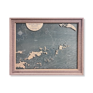 May include: A framed 3D wooden bathymetric map of the British Virgin Islands with a dark blue-grey water finish and light wood landmasses. The map features a compass rose, depth contour lines, and text reading British Virgin Islands, Fred's 60th Birthday Trip, Sailing Odyssey.