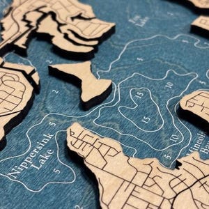 The image is a close-up of a wooden map depicting a body of water, likely a lake or river. The map is detailed and shows various landmarks and features, such as islands, coastlines, and bodies of water.