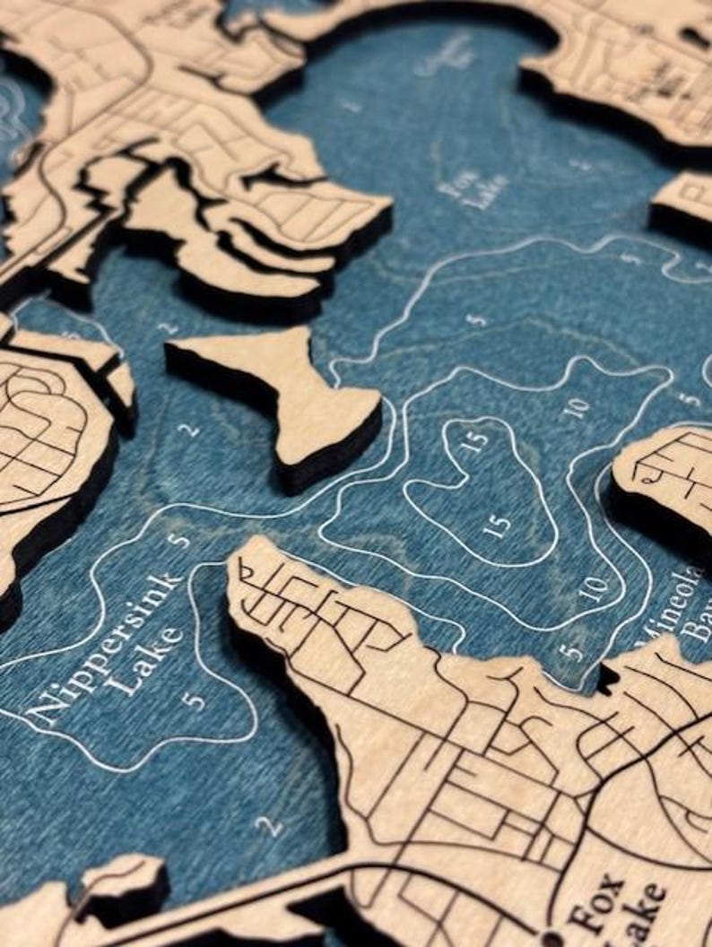 The image is a close-up of a wooden map depicting a body of water, likely a lake or river. The map is detailed and shows various landmarks and features, such as islands, coastlines, and bodies of water.