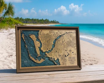 May include: A framed 3D bathymetric wood map of Cape Coral, Fort Myers, Sanibel, and Captiva in Lee County, Florida. The map features a natural wood-toned landmass contrasted against deep blue water layers, all encased in a dark wood frame.