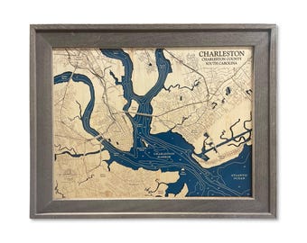 May include: A framed 16x20 inch 2D map of Charleston, South Carolina, featuring a light wood land surface and deep blue water depths. The map displays Charleston Harbor, local rivers, and roads, with the text Charleston, Charleston County, South Carolina.