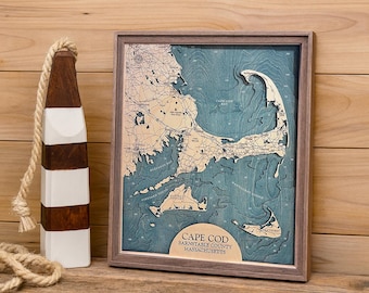 May include: A framed 3D bathymetric wood map of Cape Cod, Barnstable County, Massachusetts, featuring layered blue water depths and tan landmasses. Beside it stands a brown and white striped wooden buoy with a thick beige rope attached.