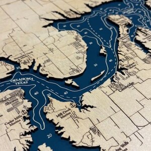 The image is a detailed map of a large body of water, likely a lake or a river, with various geographical features and labels. The map appears to be in a wooden frame, giving it a rustic and antique appearance.