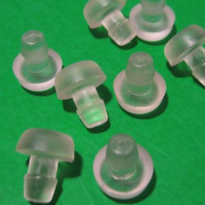 May include: A group of eight clear plastic furniture feet with a round base and a small, round, raised top. The feet are designed to protect furniture from scratching floors.