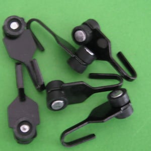 May include: Several black curtain hooks with rollers and curved hooks are displayed. The hooks are made of metal with a matte finish. The small cylindrical rollers have a silver centre. The background is a solid green colour.