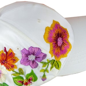 May include: White baseball cap with embroidered flowers in shades of pink, orange, yellow, and purple.