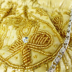 Puede incluir: Un bolso de mano de cuentas doradas con una correa de cadena plateada. El bolso est&aacute; decorado con un patr&oacute;n floral y tiene un acabado brillante.
