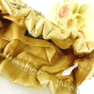 Puede incluir: Un bolso de noche de cuentas doradas con forro de sat&eacute;n y estampado floral en el exterior. El bolso tiene una correa de cadena y un cierre de broche.