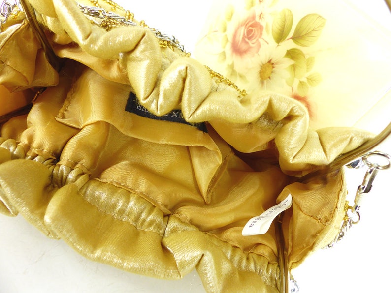 Puede incluir: Un bolso de noche de cuentas doradas con forro de sat&eacute;n y estampado floral en el exterior. El bolso tiene una correa de cadena y un cierre de broche.