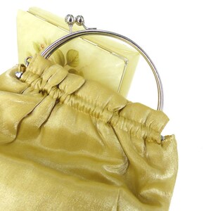 Puede incluir: Un bolso de mano de sat&eacute;n dorado con un marco de metal plateado y un cierre decorativo. El bolso tiene un dise&ntilde;o fruncido y una sensaci&oacute;n suave y lujosa.