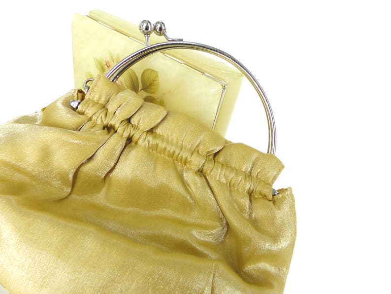 Puede incluir: Un bolso de mano de sat&eacute;n dorado con un marco de metal plateado y un cierre decorativo. El bolso tiene un dise&ntilde;o fruncido y una sensaci&oacute;n suave y lujosa.