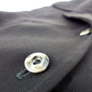 May include: A close-up of a black fabric with a silver button. The button has a raised, circular design.