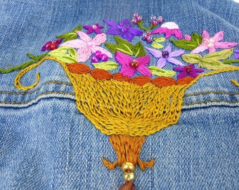 May include: A denim jacket with a colorful embroidered flower bouquet in a basket. The basket is made of brown yarn and has a beaded dangle.