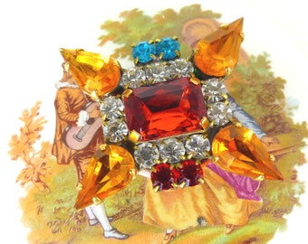 Centro de cristal rojo brillante con detalles de cristal mandarina y aguamarina. Broche magnético para bufanda. Botón trasero de seda Mag TAK™. Embalaje gratuito.