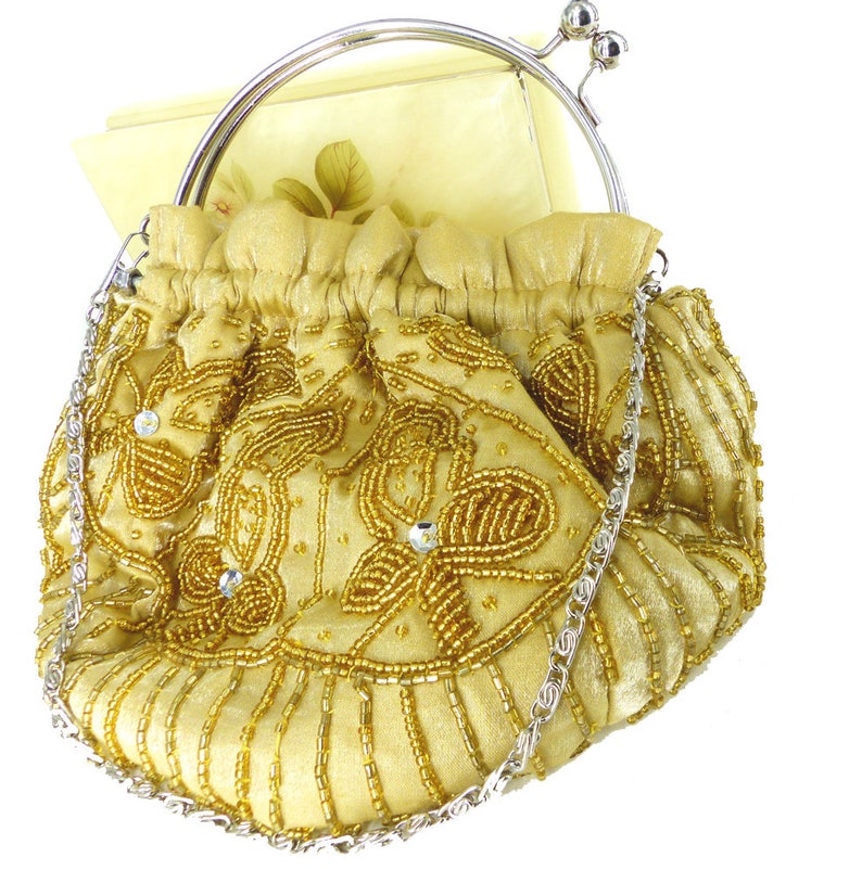 Puede incluir: Un bolso de noche de cuentas doradas con una correa de cadena plateada y un cierre plateado. El bolso est&aacute; decorado con un patr&oacute;n floral.
