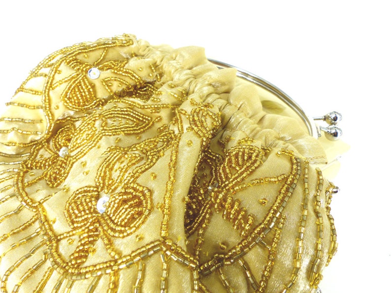 Puede incluir: Un bolso de mano de cuentas doradas con cierre de plata. El bolso est&aacute; decorado con un patr&oacute;n floral y tiene un detalle de flecos.