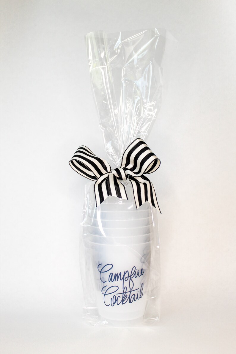 May include: A set of clear plastic cups with a black and white striped ribbon tied around them. The cups are wrapped in clear plastic and have the text "Campfire Cocktail" printed on them in blue.