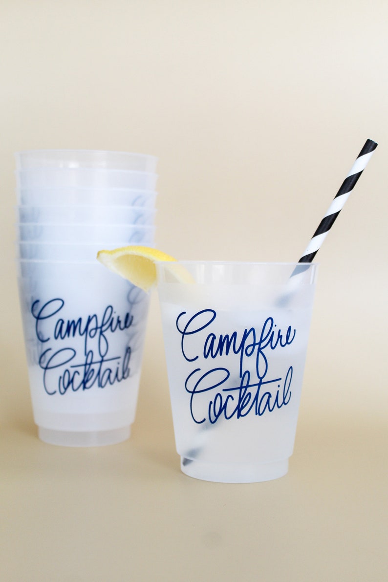 May include: A set of clear plastic cups with a black and white striped straw. The cups have the text "Campfire Cocktail" printed on them in blue. A lemon wedge is in the cup on the right.