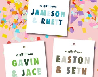 Könnte beinhalten: Drei weiße Geschenkanhänger mit buntem Text. Der obere Anhänger sagt "ein Geschenk von JAMESON & RHETT" in Blau, Hellblau und Weiß. Der mittlere Anhänger sagt "ein Geschenk von GAVIN & JACE" in Grün und Hellgrün. Der untere Anhänger sagt "ein Geschenk von EASTON & SETH" in Braun, Grau und Hellgrün.