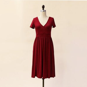 May include: A burgundy midi dress with a V-neckline and short sleeves. The dress has a wrap-style bodice and a flowing skirt.