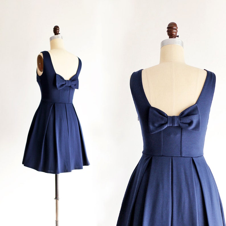 May include: A navy blue dress with a bow detail on the back. The dress has a fitted bodice and a flared skirt. The dress is sleeveless and has a scoop neckline. The dress is displayed on a mannequin.