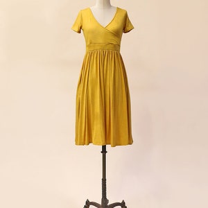 May include: A mustard yellow wrap dress with short sleeves and a gathered skirt. The dress is on a mannequin.