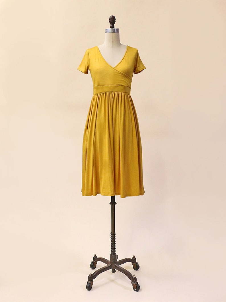 May include: A mustard yellow wrap dress with short sleeves and a gathered skirt. The dress is on a mannequin.