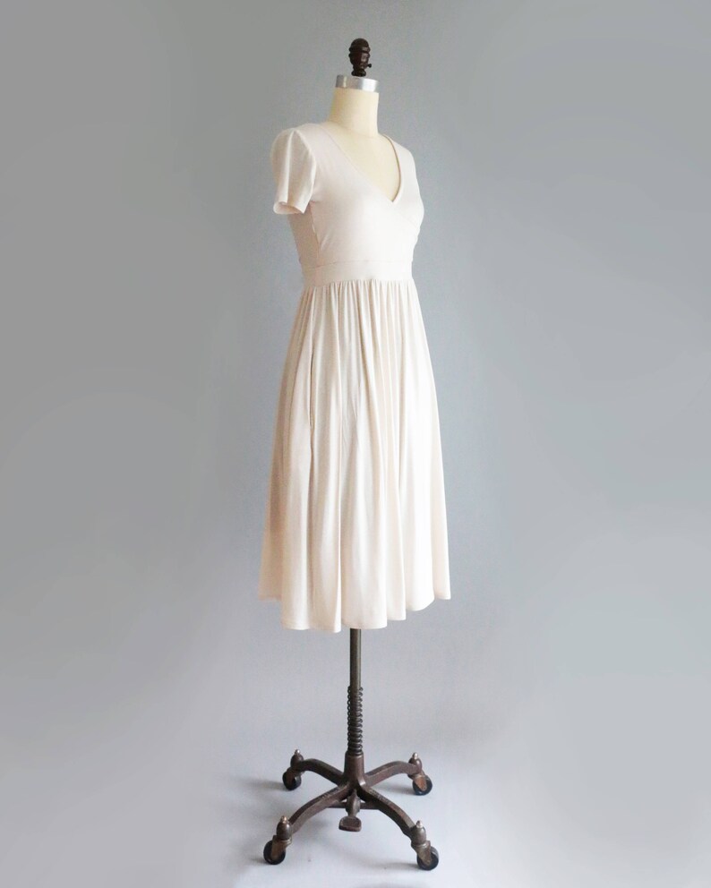 May include: A simple, off-white, knee-length dress with a V-neckline and short sleeves. The dress is made of a soft, flowing fabric and has a gathered skirt.