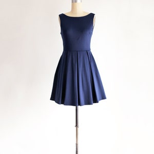 May include: A navy blue sleeveless dress displayed on a mannequin. The dress features a boat neckline, fitted bodice, and a flared skirt with pleats. The dress is made of a smooth fabric and is suitable for various occasions.