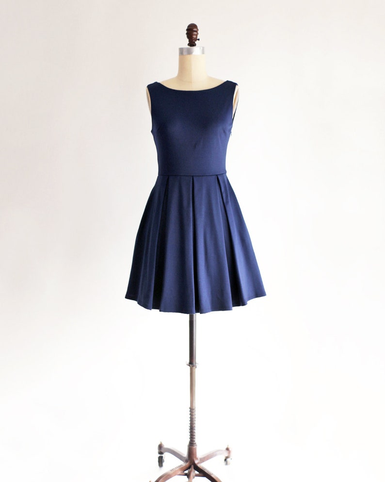 May include: A navy blue sleeveless dress displayed on a mannequin. The dress features a boat neckline, fitted bodice, and a flared skirt with pleats. The dress is made of a smooth fabric and is suitable for various occasions.