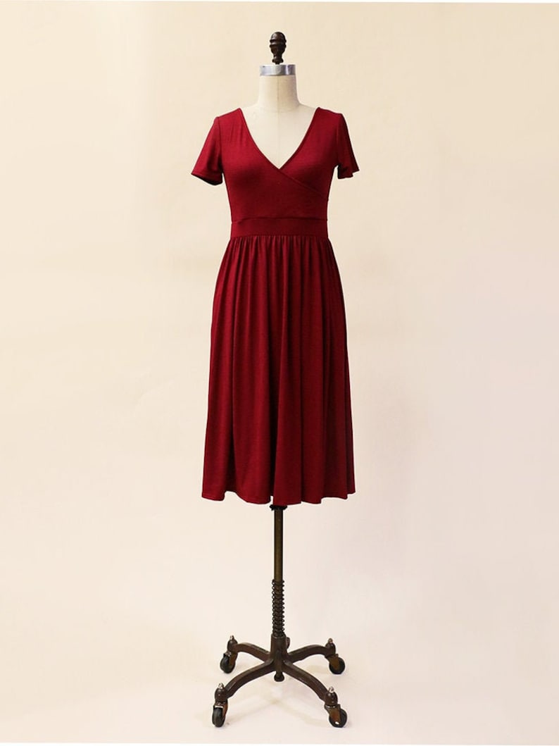 May include: A burgundy midi dress with a V-neckline and short sleeves. The dress has a wrap-style bodice and a flowing skirt.