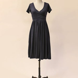 May include: A charcoal gray wrap dress with short sleeves and a V-neckline. The dress has a fitted bodice and a flowing skirt.