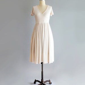 May include: A simple, off-white, knee-length dress with a V-neckline and short sleeves. The dress has a wrap-style bodice and a flowing skirt.