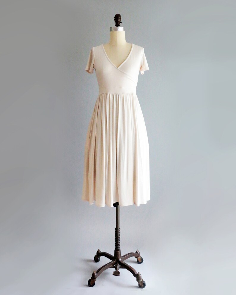 May include: A simple, off-white, knee-length dress with a V-neckline and short sleeves. The dress has a wrap-style bodice and a flowing skirt.