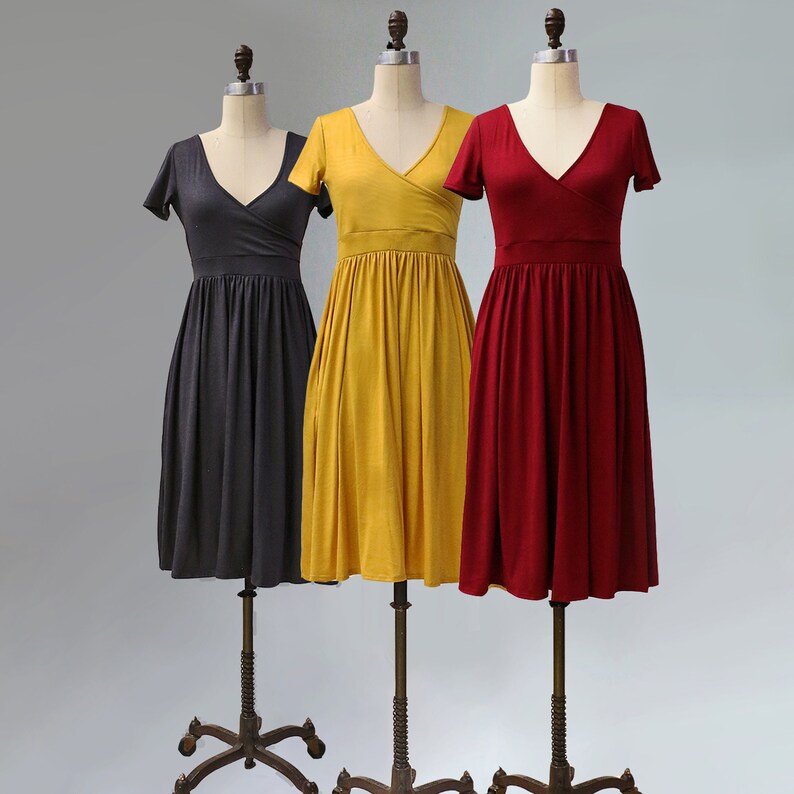 May include: Three dresses on mannequins, a dark gray dress, a mustard yellow dress, and a burgundy red dress. All three dresses have a V-neck and short sleeves.