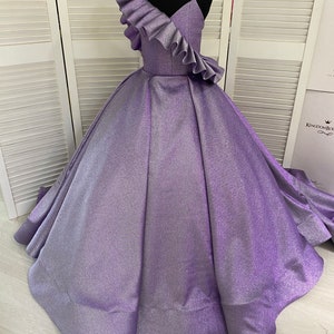 May include: A purple sparkly sleeveless dress with a ruffled one-shoulder neckline. The dress has a full skirt and is perfect for a special occasion.